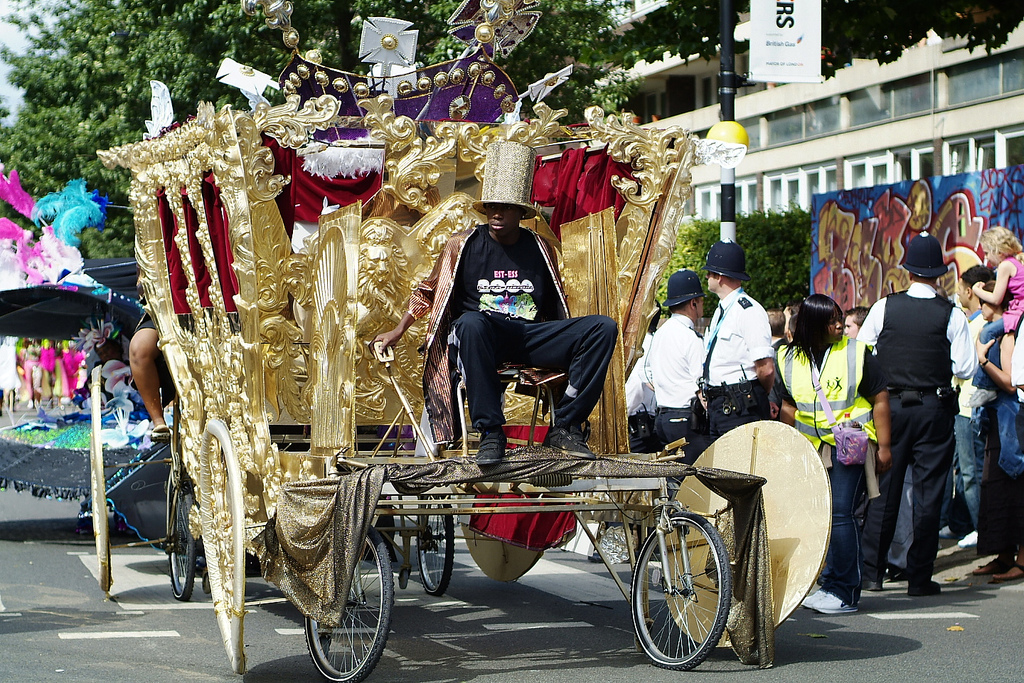 Auf dem Bild ist ein Fahrzeug und Menschen bei der Notting-Hill-Karneval Feier zu sehen