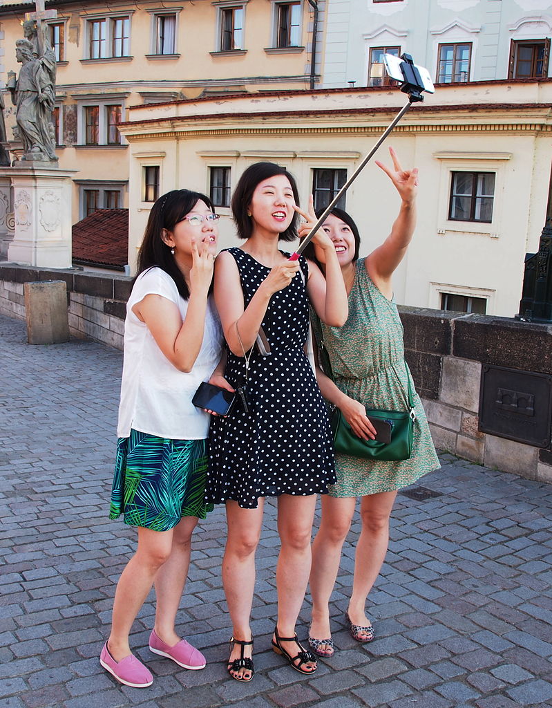 Auf dem Bild sind Frauen mit einem Selfie stick zu sehen. Sie machen ein Foto von sich.