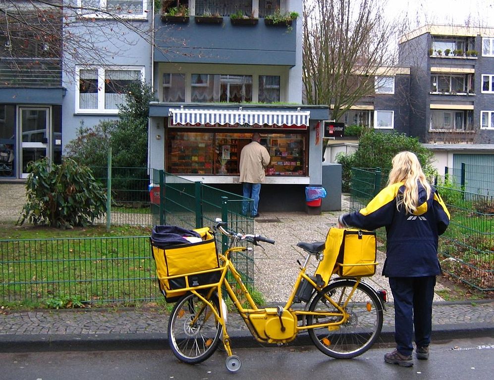 Auf dem Bild ist eine Briefträgerin mit Fahrrad zu sehen