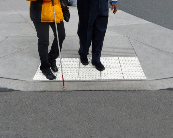 Auf dem Bild sind zwei Personen zu sehen. Eine Person benutzt einen Blindenstock.