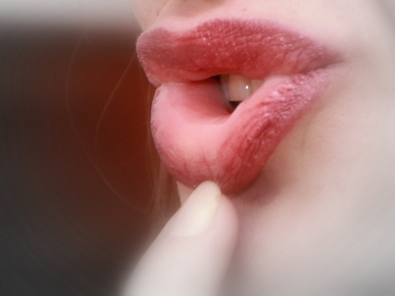 Auf dem Bild ist der Mund einer Frau zu sehen. Vor den Lippen ist ein Finger.