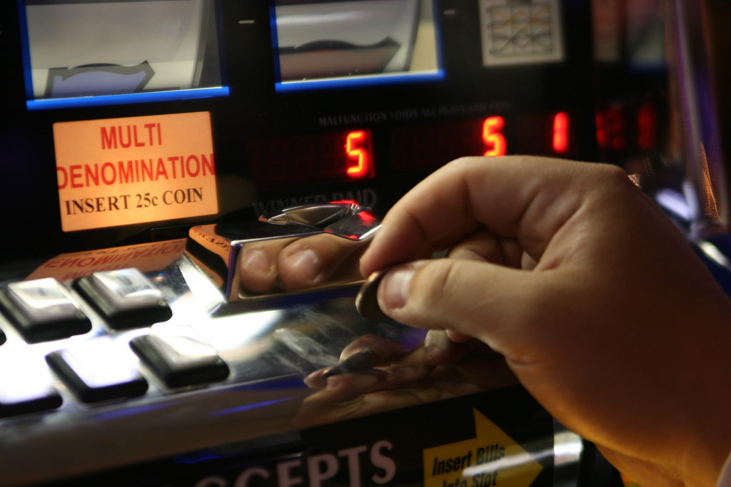 Auf dem Bild ist ein Spielautomat zu sehen. Es wird eine Münze eingeworfen.